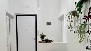 A hallway with a white door, a black chair, a small table with a woven placemat, and a wall-mounted plant. - Lucky Corner - Elegant Stay (Taranto)