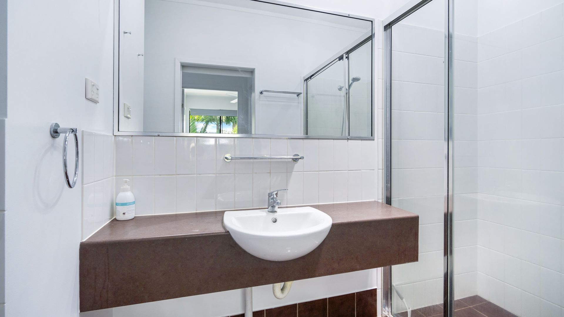 Une salle de bain moderne avec un lavabo blanc, un miroir et une cabine de douche en verre.