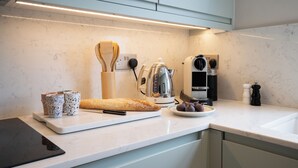 A modern kitchen with a marble countertop, a bread loaf, a coffee maker, and a kettle. - Light filled Apartment - newly renovated (London)