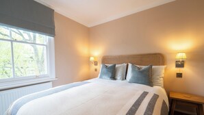 A neatly made bed with a striped blanket, two bedside lamps, and a wooden nightstand. - Light filled Apartment - newly renovated (London)