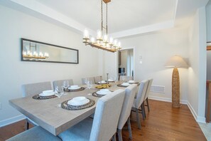 Une salle à manger avec une table rectangulaire dressée pour six personnes, un lustre, un grand lampadaire et un miroir au mur.