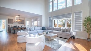 A spacious living area with a large L-shaped sectional sofa, a round coffee table, and a dining area with a kitchen in the background. - Muskoka Hills - Four Bedroom Cottage, Sleeps 8 (Huntsville)