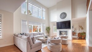 A spacious living room with a large sofa, a coffee table, and a fireplace. There is a television mounted on the wall and a clock above it. - Muskoka Hills - Four Bedroom Cottage, Sleeps 8 (Huntsville)