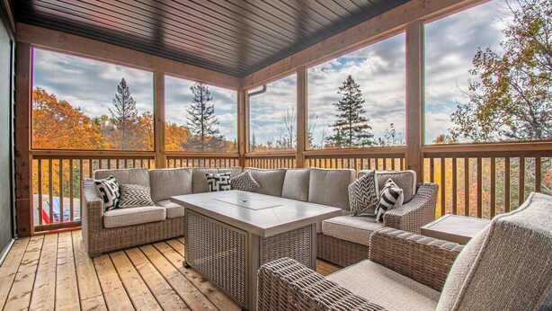 A covered outdoor seating area with wicker furniture and large windows offering views of trees and sky. - Muskoka Hills - Four Bedroom Cottage, Sleeps 8 (Huntsville)