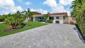 A two-story house with a red-tiled roof, a paved driveway, and a well-maintained lawn with palm trees.