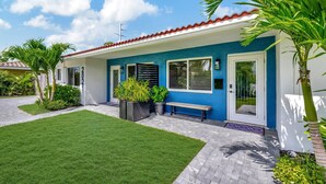 A blue house with a red roof, a front door, and a bench outside.