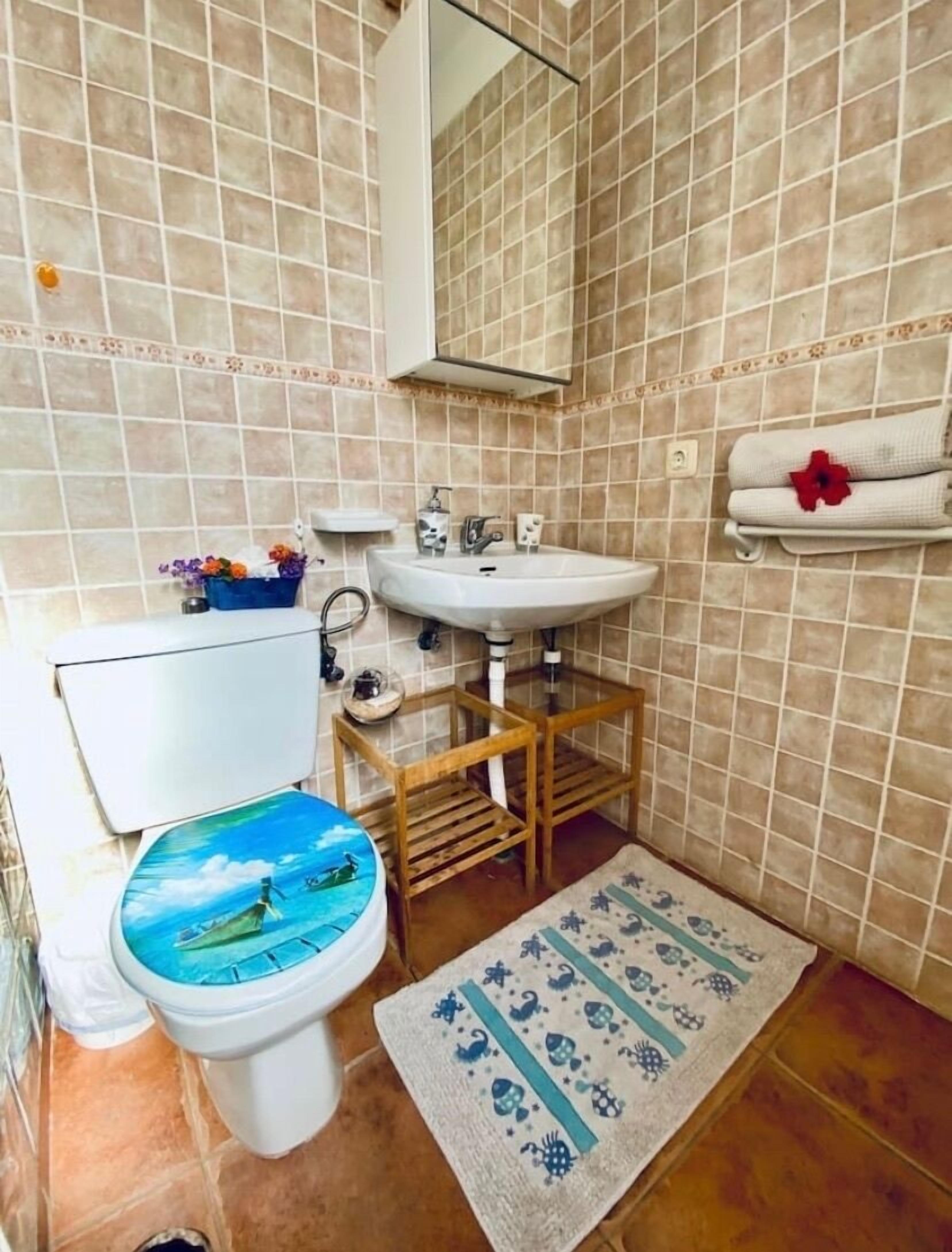 A bathroom with a toilet, sink, mirror, and tiled walls.