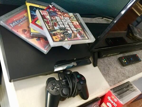 En speluppställning med en PlayStation-kontroller, en PlayStation 3-konsol och en samling spelomslag på ett bord.