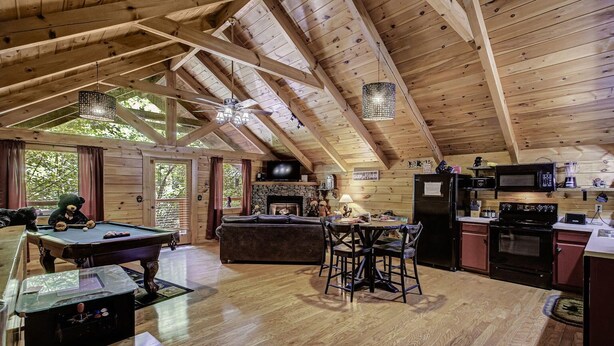 Une cabane en bois spacieuse, dotée d’une table de billard, d’un coin salon confortable, d’une cuisine équipée d’appareils électroménagers modernes et d’une cheminée.