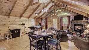 Un intérieur de chalet chaleureux avec un plafond en bois, une cheminée, une table de billard et un coin repas.