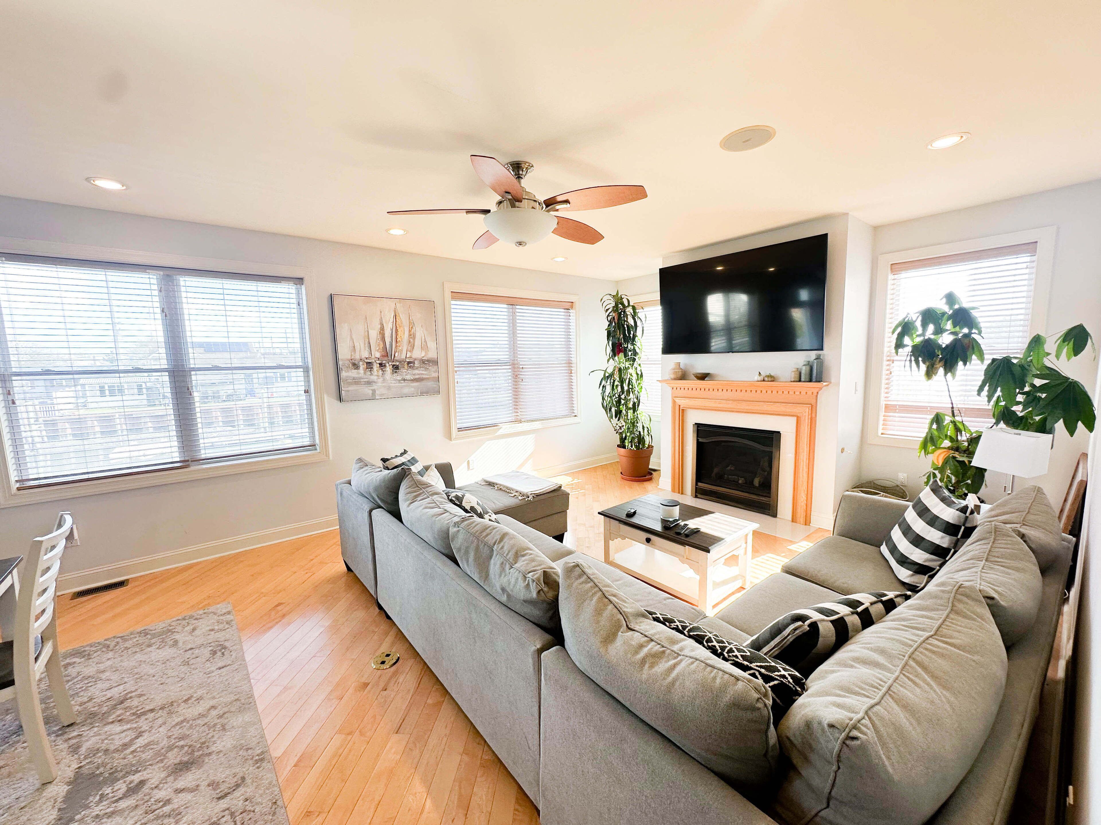 A modern living room with a gray sofa, a fireplace, a ceiling fan, and a large TV.