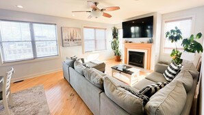 Una sala de estar moderna con un sofá gris, una chimenea, un ventilador de techo y un televisor grande.