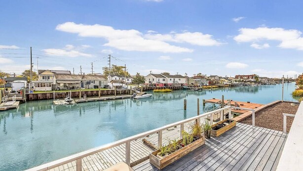 Una propiedad frente al agua con muelle, barcos y una terraza de madera con macetas.