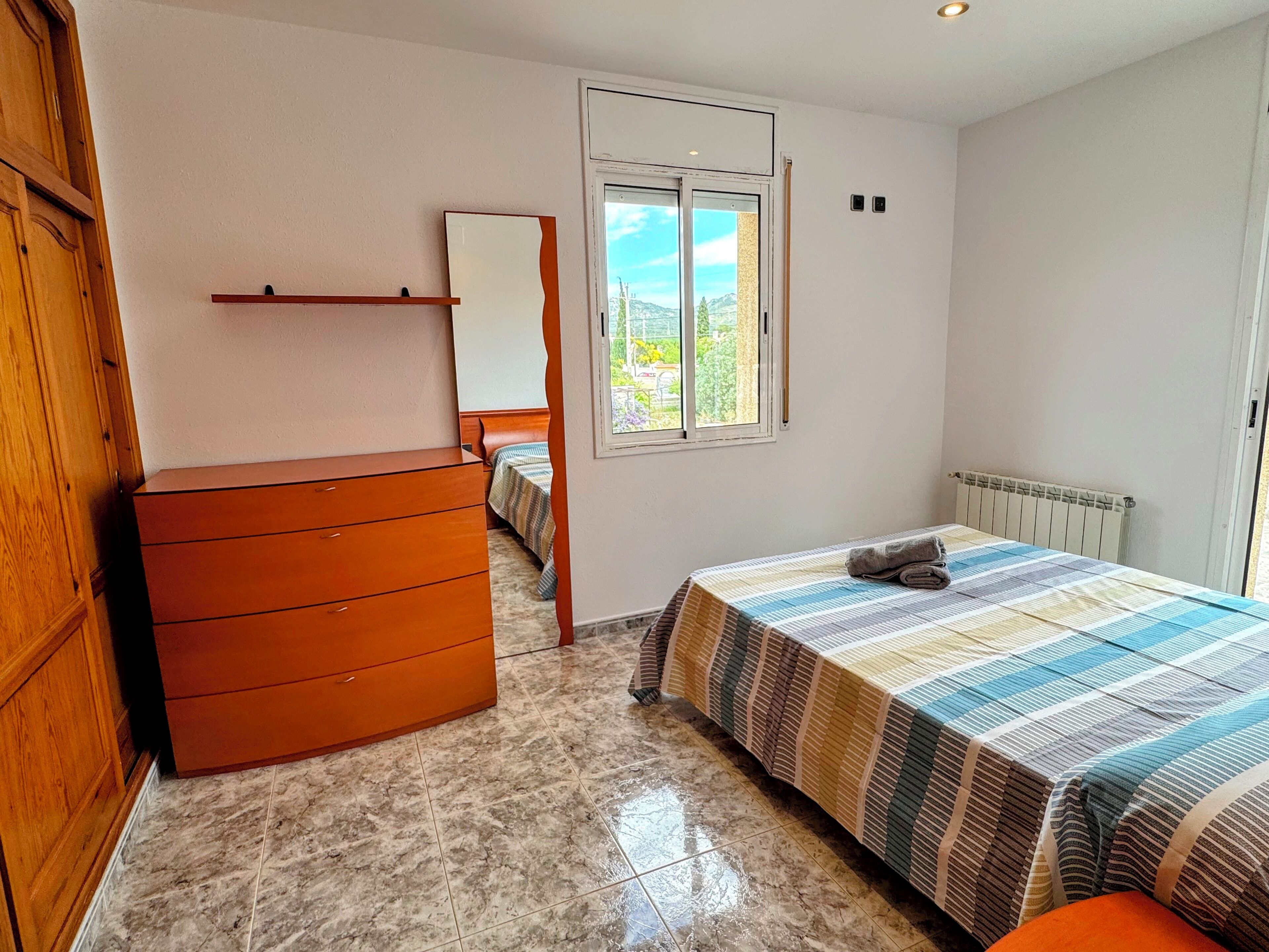 Una camera da letto con un letto, una cassettiera, uno specchio, una finestra e un termosifone.