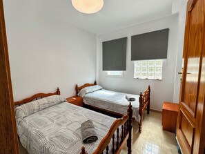 A bedroom with two beds, a wooden wardrobe, and a window with blinds.
