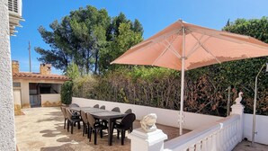 Un patio al aire libre con una mesa, sillas, un paraguas grande y una barandilla blanca.