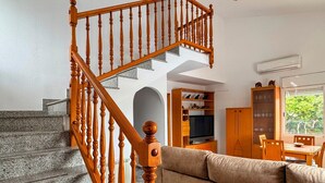 Una escalera con barandillas de madera, una sala de estar con sofá, televisor y un comedor con sillas y mesa.