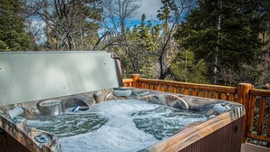 Un jacuzzi con revestimiento de madera, rodeado por una terraza de madera y árboles.