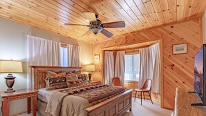Un dormitorio acogedor con techo de madera, una cama con ropa de cama estampada, una mesita de noche, una silla y un televisor.