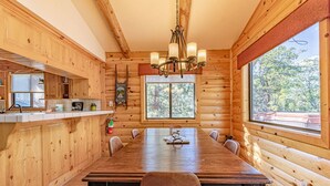 Interior de una cabaña de troncos con una gran mesa de comedor, paredes de madera y una araña.