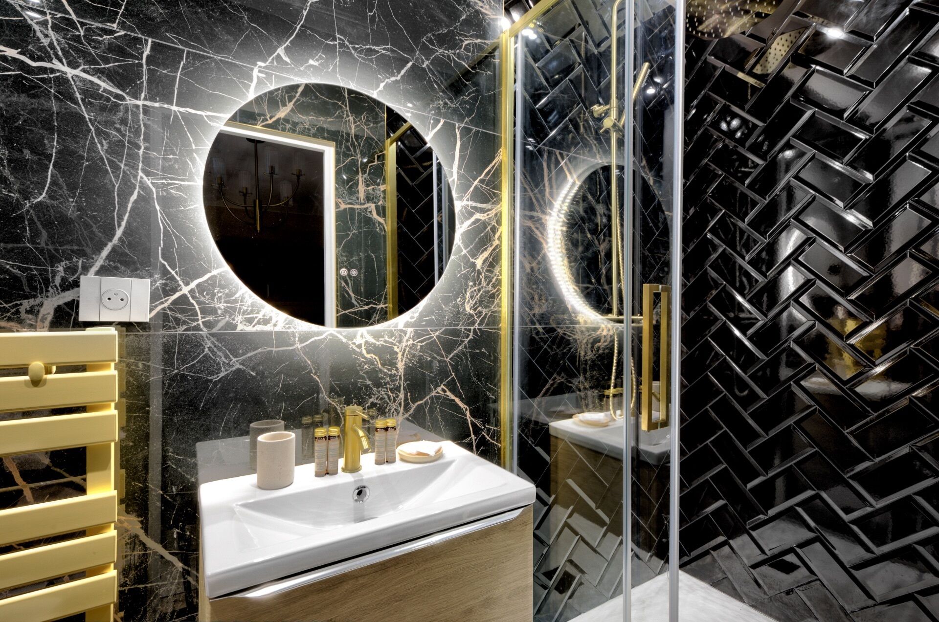 Un baño moderno con salpicadero de mármol, un espejo redondo, un lavabo con artículos de aseo y un mueble de tocador de madera.