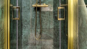 A modern shower with a handheld showerhead and a fixed wall-mounted showerhead, surrounded by glass panels and marble tiles. - Maison Belleville (Paris)