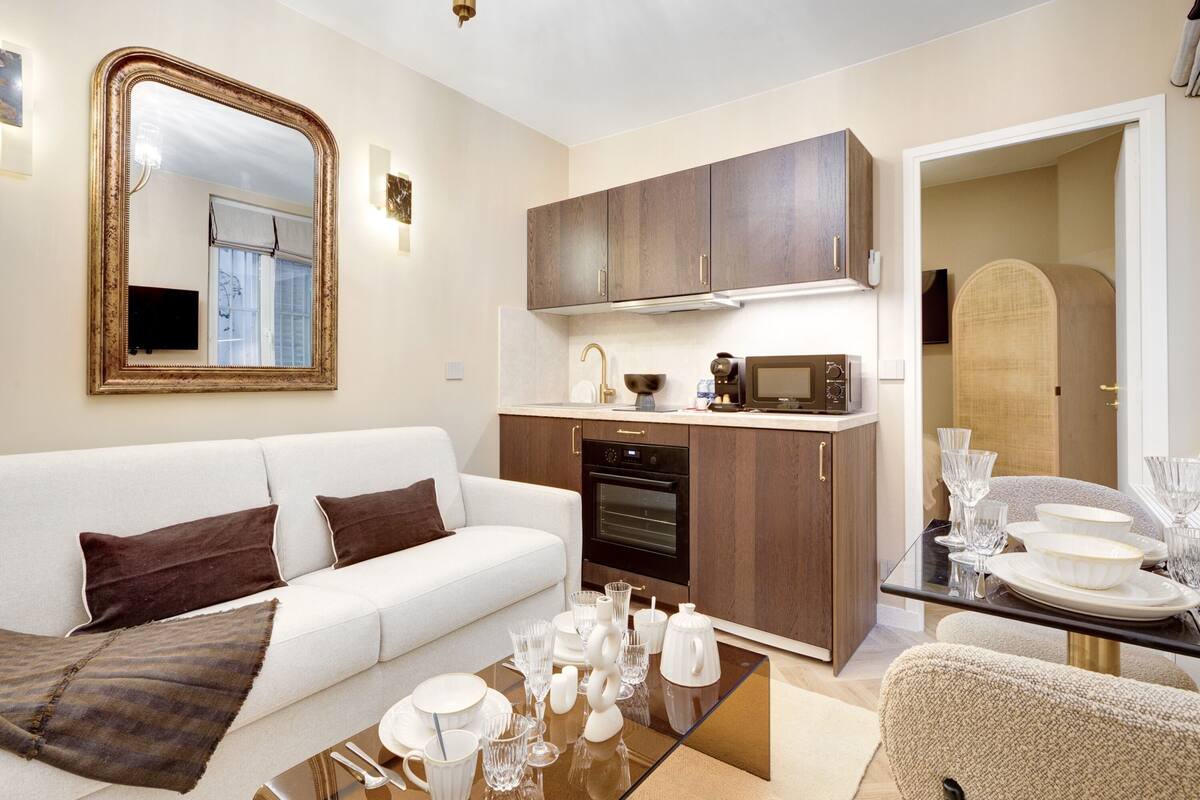 A modern living room with a white sofa, a glass coffee table, and a kitchen area with wooden cabinets and a microwave.