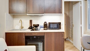A compact kitchen with wooden cabinets, a built-in oven, a microwave, and a coffee maker. - Maison Belleville (Paris)