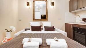 A hotel room with a large bed, a mirror above it, a small kitchen area, and a vase with flowers on the side table. - Maison Belleville (Paris)