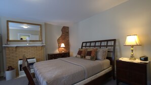 A bedroom with a bed, a nightstand, a lamp, a mirror, and a brick wall.