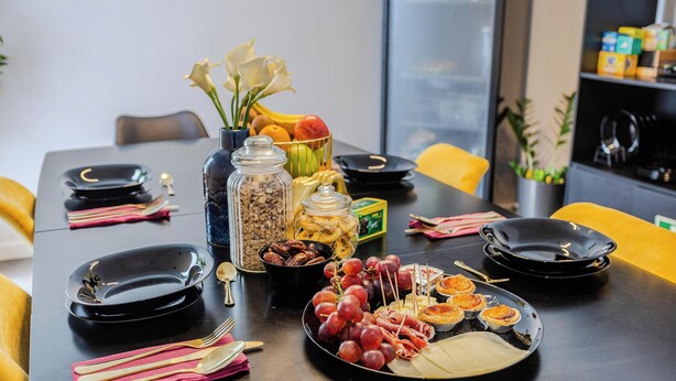 A dining table set with plates, cutlery, and a variety of food items including grapes and pastries.