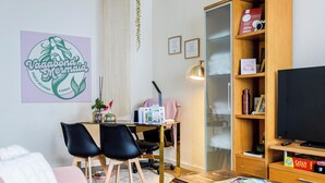 A living room with a dining table, two chairs, a bookshelf, a television, and a framed certificate on the wall.
