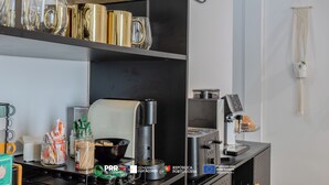 A kitchen area with shelves holding glassware, a coffee machine, and various kitchen utensils.