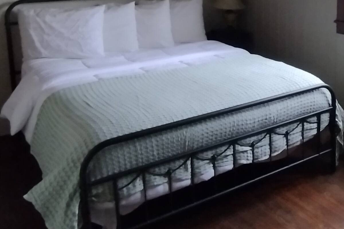 Ein Bett mit Metallgestell, weißer Bettwäsche und einem Deckenventilator.