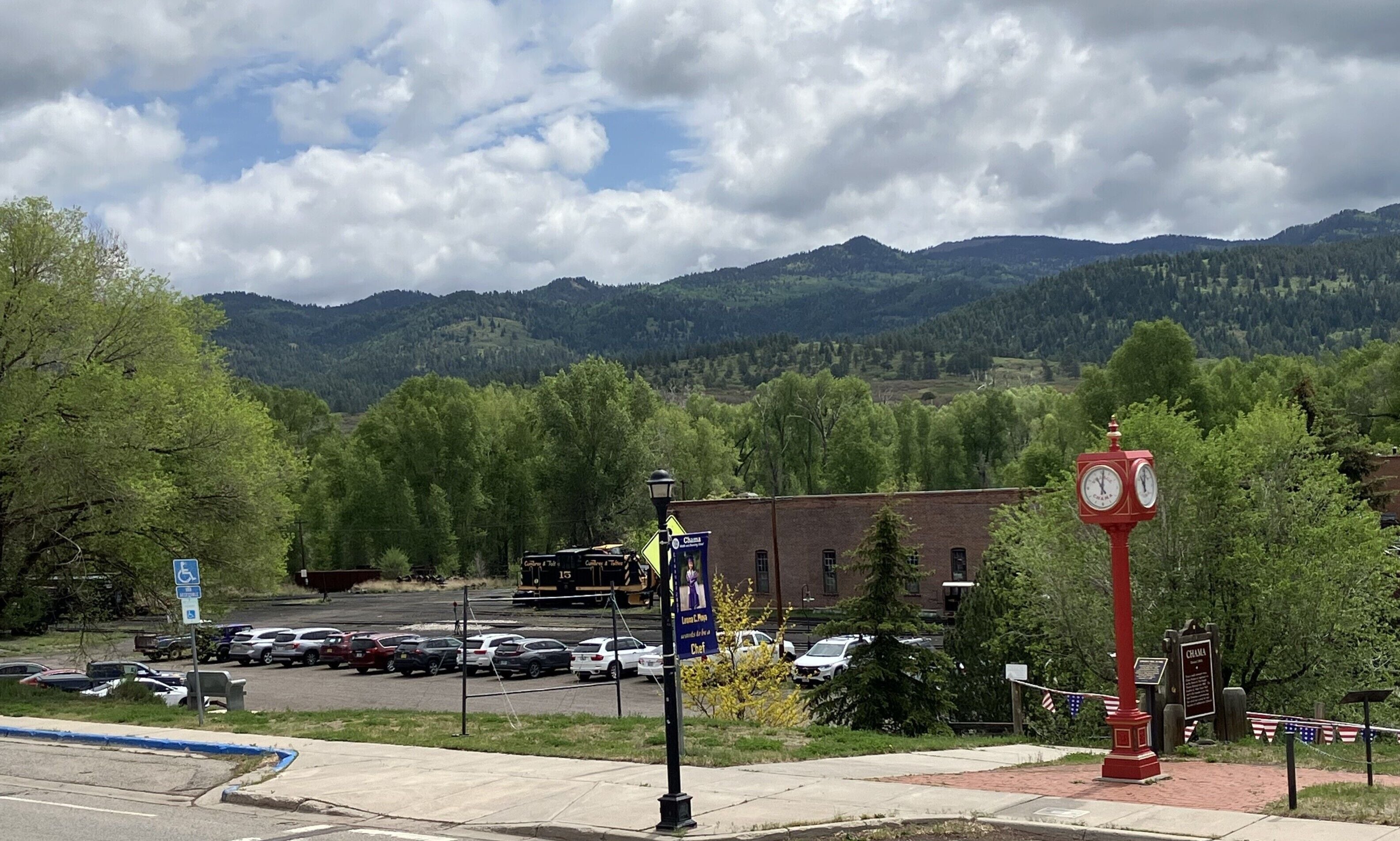 A parking lot with cars, a clock, and a mountain backdrop.