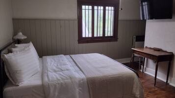 Un dormitorio con cama, escritorio, silla, ventana y televisor en la pared.