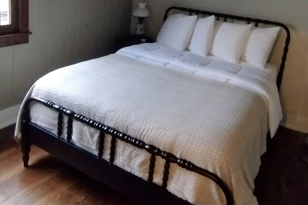 Ein Schlafzimmer mit Bett, Deckenventilator, Nachttisch mit Lampe und Fenster.
