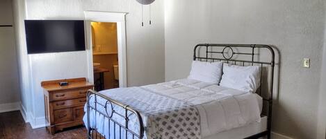 A bedroom with a metal bed frame, a ceiling fan, a wooden dresser, and a television on the wall.