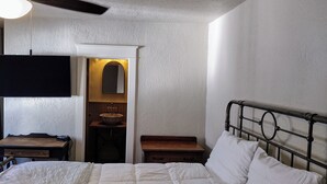 A bedroom with a bed, a nightstand, a desk, a mirror, and a ceiling fan.