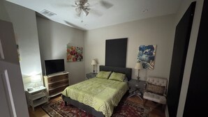 Ein Schlafzimmer mit einem Bett, einem Fernseher, zwei Nachttischen, einem Deckenventilator und Kunstwerken an den Wänden.