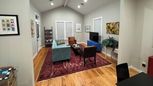 Ein geräumiges Wohnzimmer mit hohen Decken, Holzböden, einem blauen Sofa, einem Esstisch mit Stühlen und einem Fernseher.