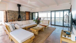A spacious living area with a stone wall, a large sofa set, a wooden coffee table, and a view through large windows. - Amazing mountain top villa! (Castries)
