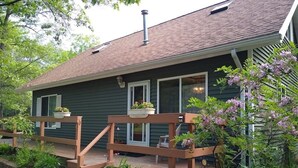 A house with a wooden deck, a covered porch, and a garden with various plants and flowers.