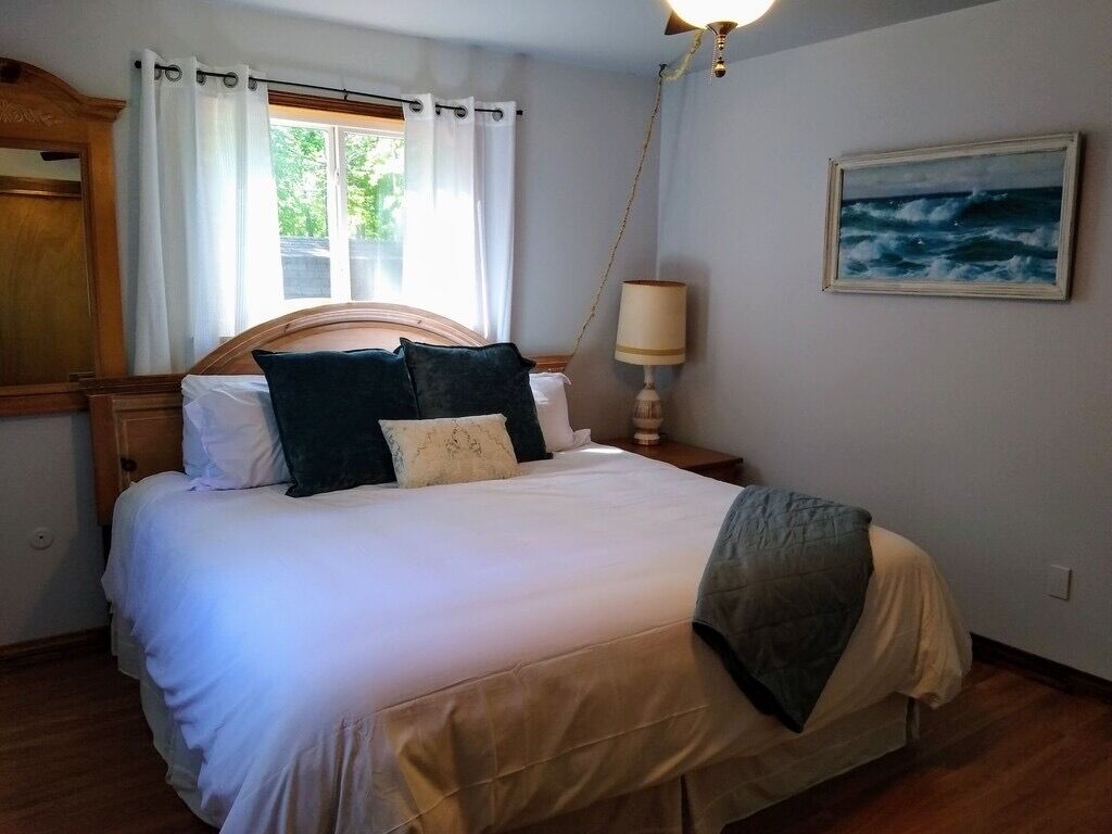 A neatly made bed with a wooden headboard, a bedside lamp, and a painting of the ocean on the wall.