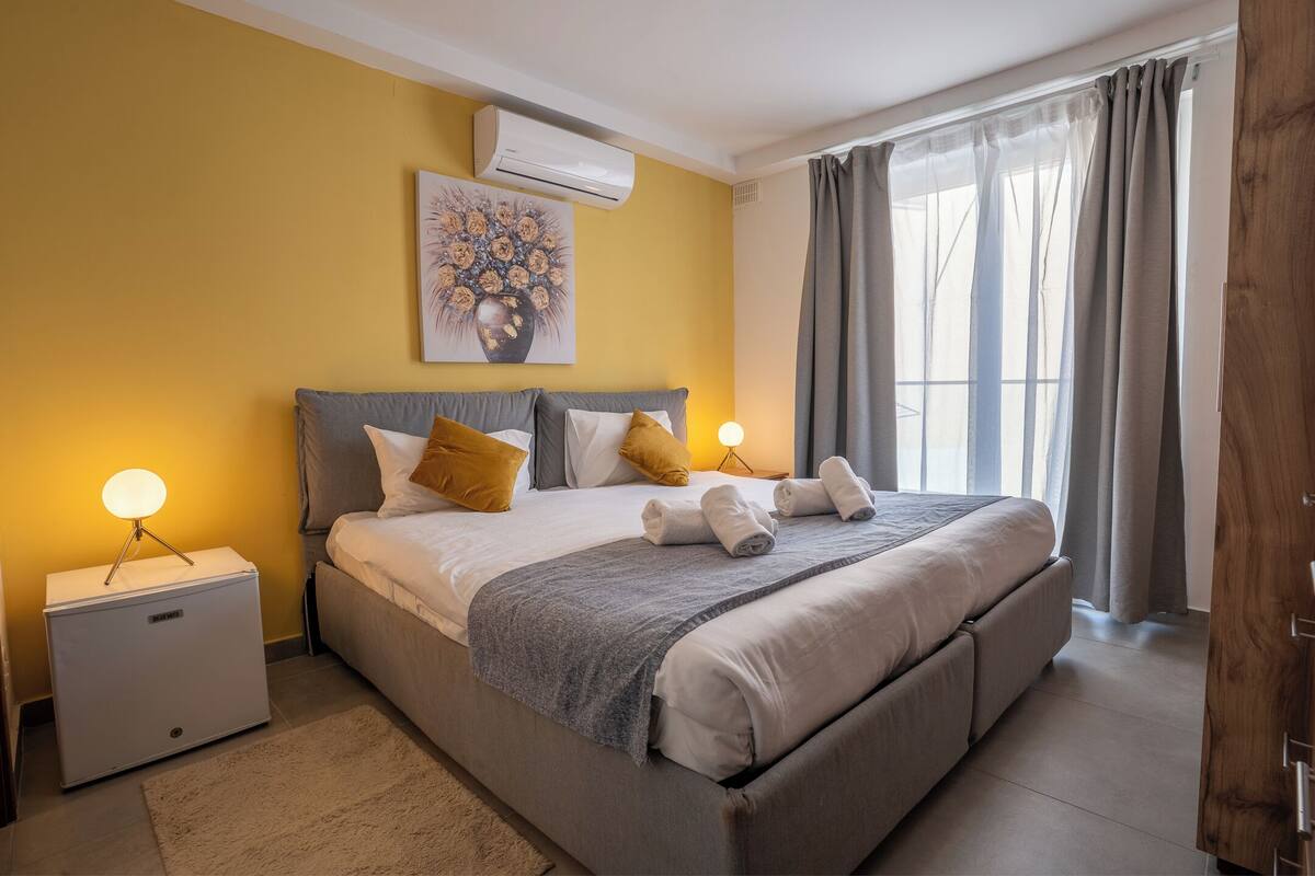 Una cama bien hecha con almohadas, una lámpara de noche y una mesita de noche con lámpara.