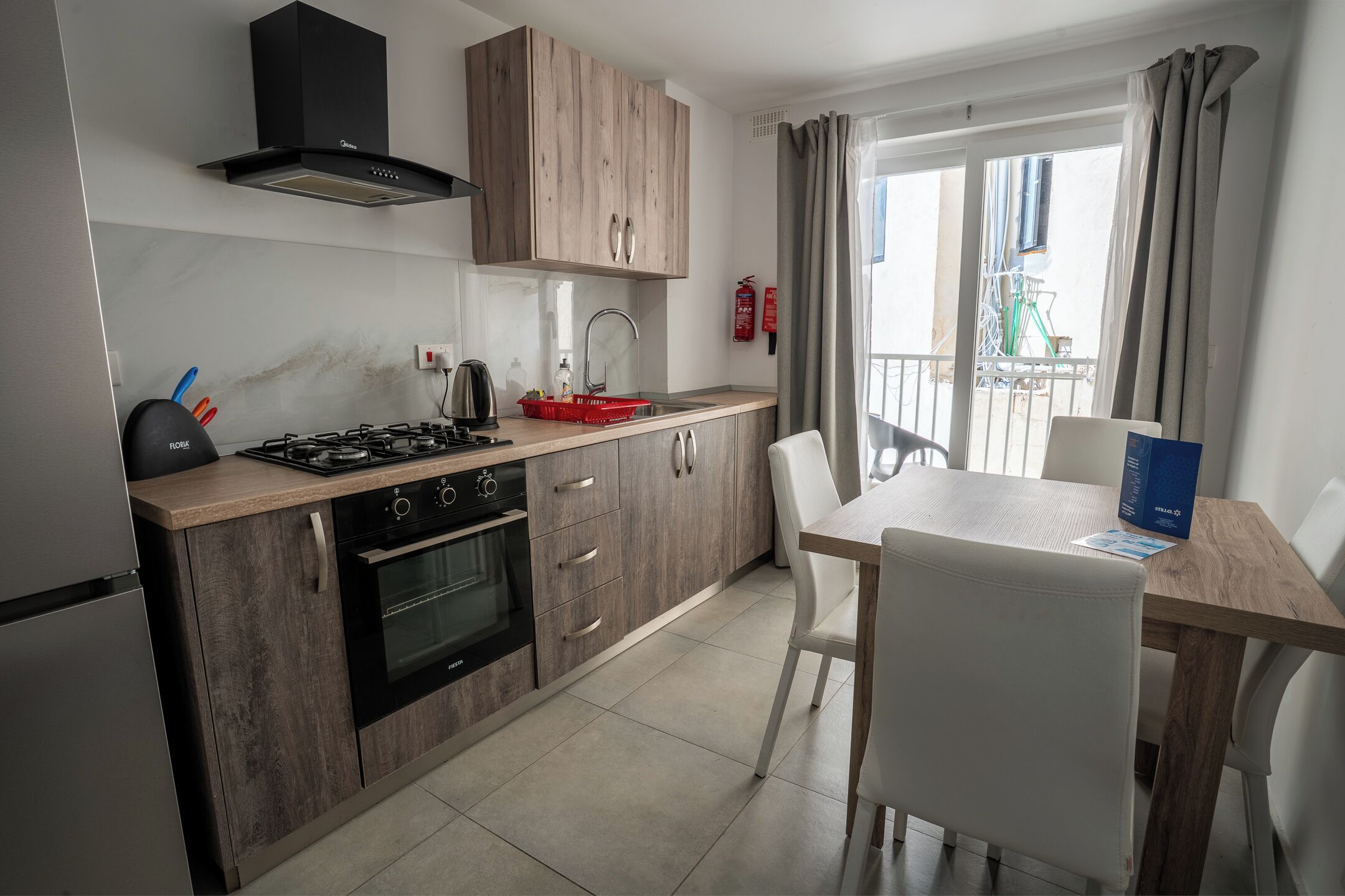 Cocina moderna con estufa a gas, horno y alacenas de madera. Hay una mesa de comedor con sillas y vistas al exterior.