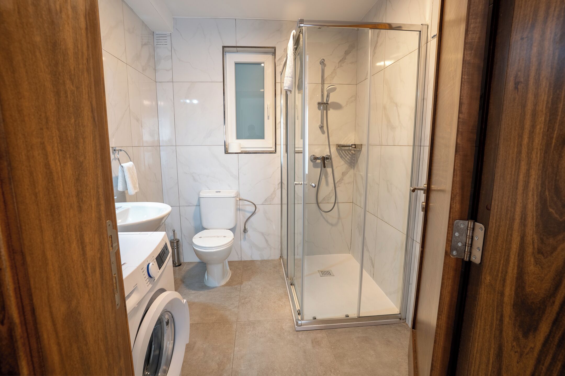 A bathroom with a glass-enclosed shower, a toilet, a washing machine, and a sink.
