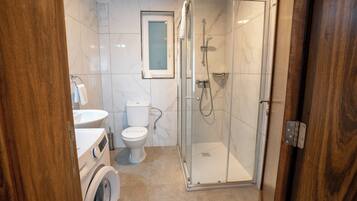 A bathroom with a glass-enclosed shower, a toilet, a washing machine, and a sink.