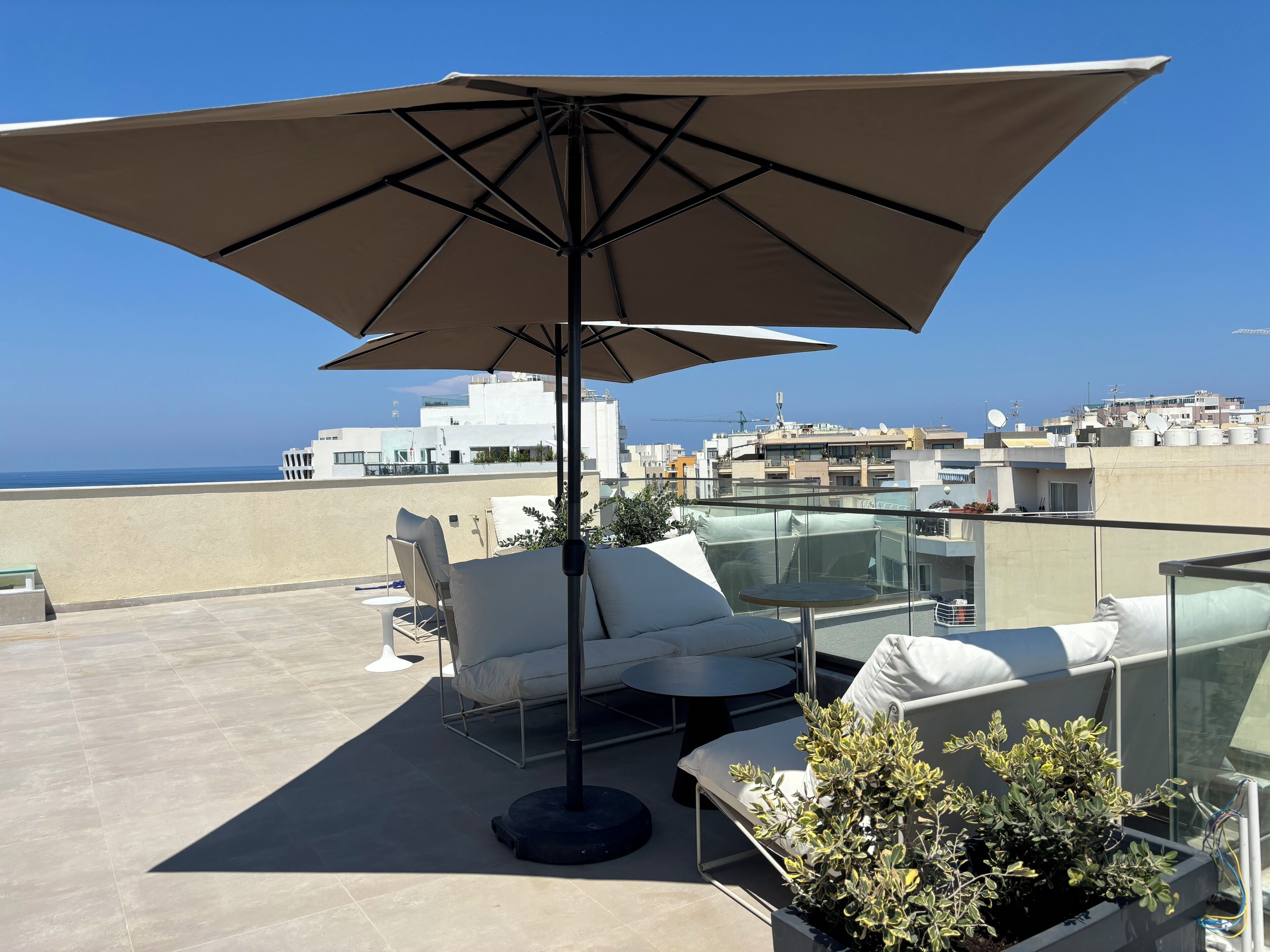 A rooftop terrace with a large umbrella, white lounge chairs, and a small table.