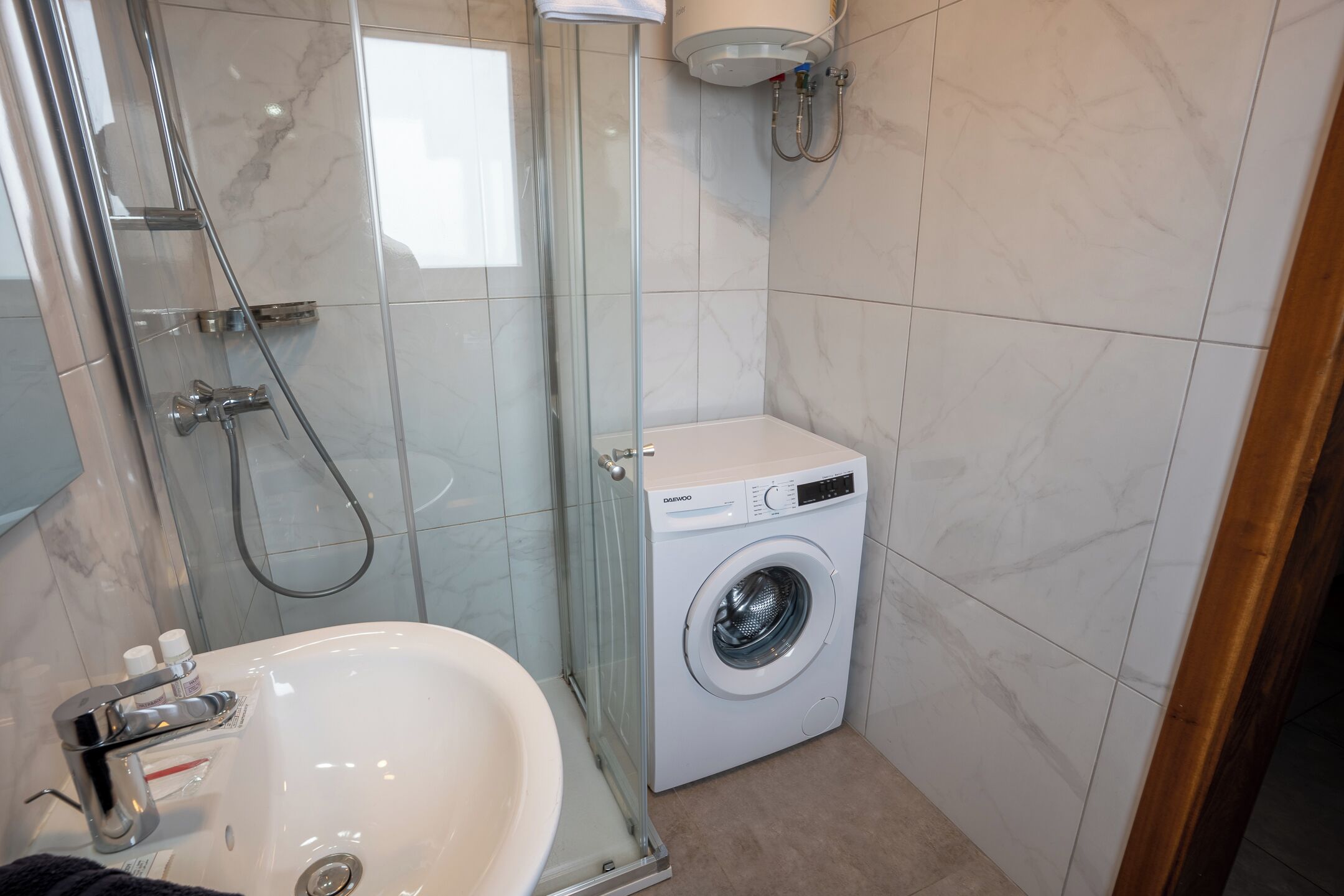 A bathroom with a glass-enclosed shower, a sink, and a front-loading washing machine.